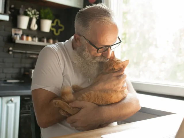 Un homme fait un câlin à son chat dans sa cuisine.