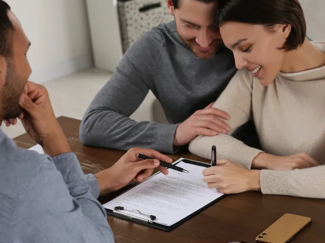 Un couple heureux signe le compromis de vente pour l'achat de leur nouvelle maison chez leur notaire.