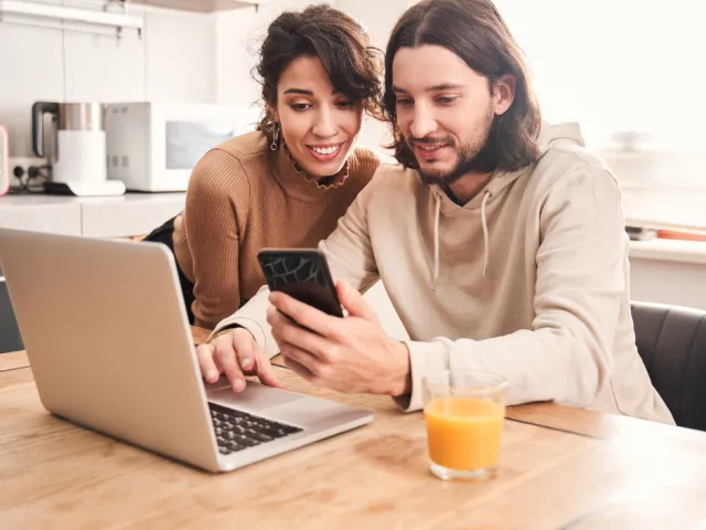 Un couple heureux pose une enchère sur un bien immobilier sur le site de vente immobilière en ligne Biddit.be.